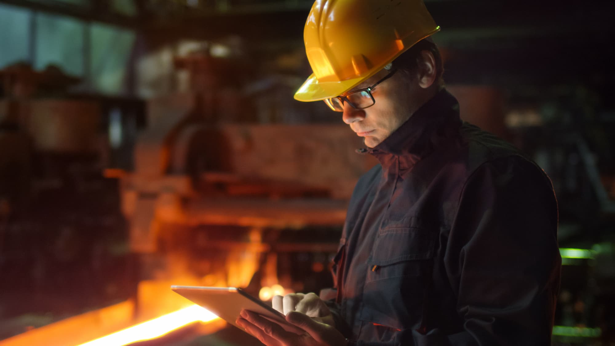 Engineer in glasses is utilizing a tablet PC in an industrial setting. 