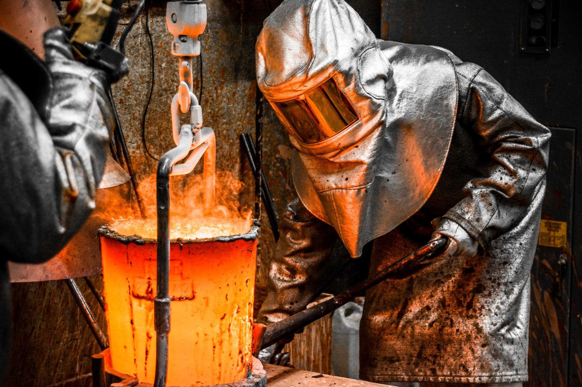 Workers in safety gear handling a crucible containing molten metal. 